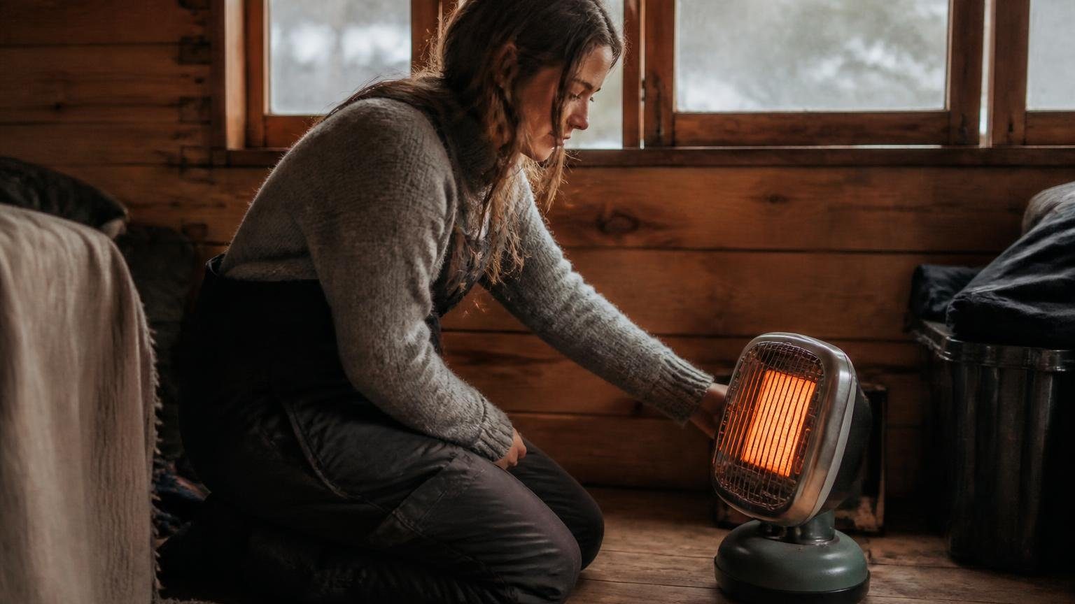 Homeowner running a small portable propane heater indoors near a cracked-open window in a cabin